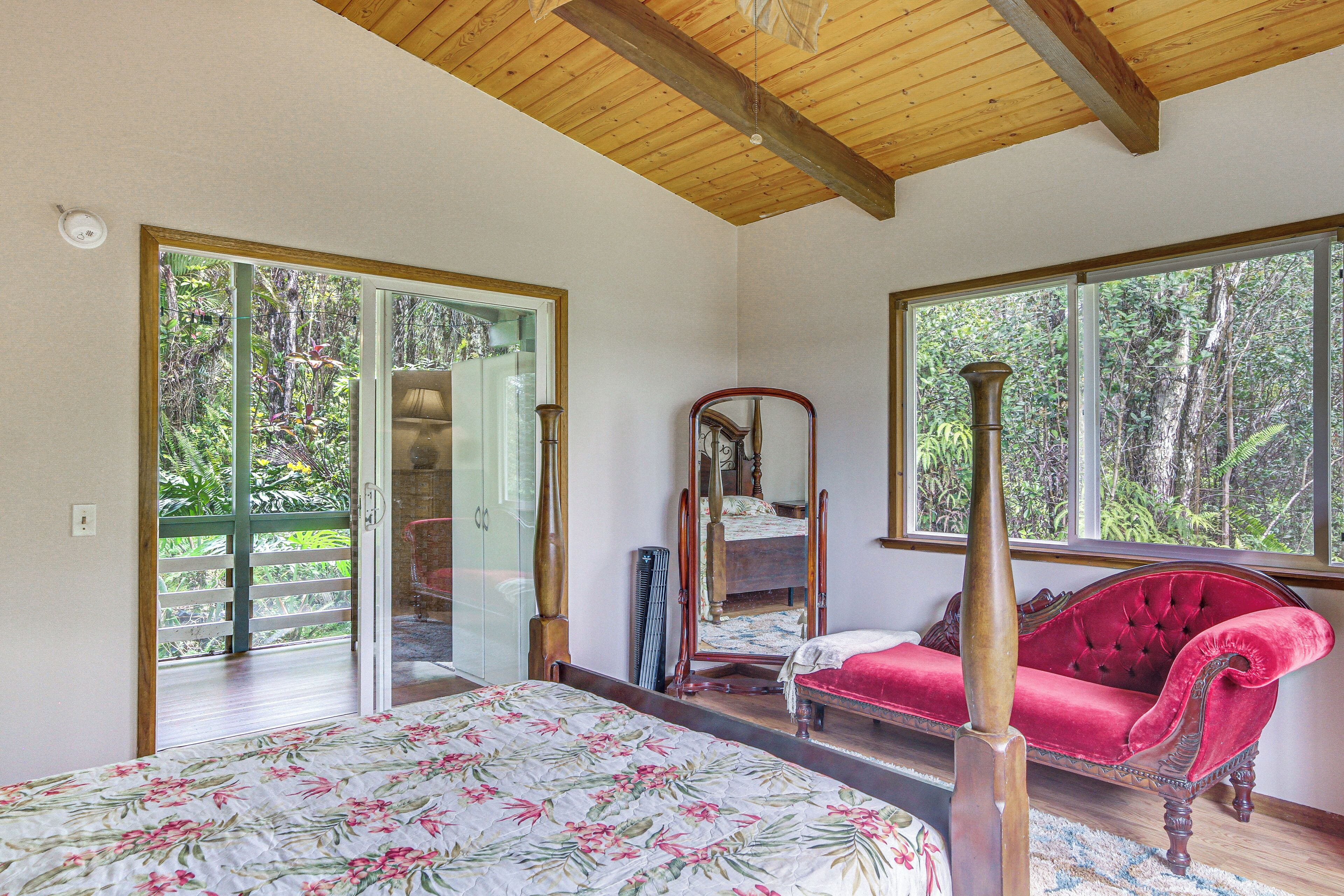 A bedroom with a bed, a red sofa, a large mirror, and a view of the outdoors through a sliding door.