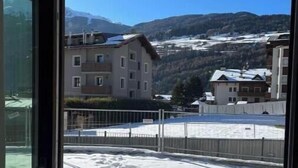 A view from a balcony with a snow-covered ground, buildings in the background, and mountains. - 2 - Bormio Al Pradais Apartments - WEST Garden (Bormio)