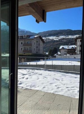 A view from a balcony with a snow-covered ground, buildings in the background, and mountains. - 2 - Bormio Al Pradais Apartments - WEST Garden (Bormio)