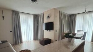 A modern kitchen with a central island, a flat-screen TV mounted on the wall, and a dining area with a table and chairs. - 2 - Bormio Al Pradais Apartments - WEST Garden (Bormio)