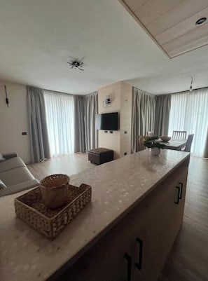 A modern kitchen with a central island, a flat-screen TV mounted on the wall, and a dining area with a table and chairs. - 2 - Bormio Al Pradais Apartments - WEST Garden (Bormio)