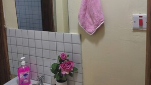 Une salle de bain avec un lavabo, un miroir, une serviette rose, un cadre avec une citation et un rosier en pot.