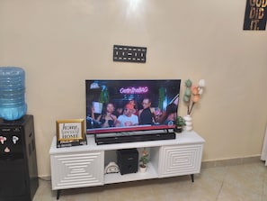 A television on a white cabinet with a framed sign, a water dispenser, and a small potted plant. - Charming 1-bedroom apartment in vibrant Eastern bypass perfect for your stay (Nairobi)