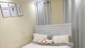 Une chambre à coucher bien rangée, avec un lit, des oreillers, une table de chevet, un luminaire fixé au mur et une porte.