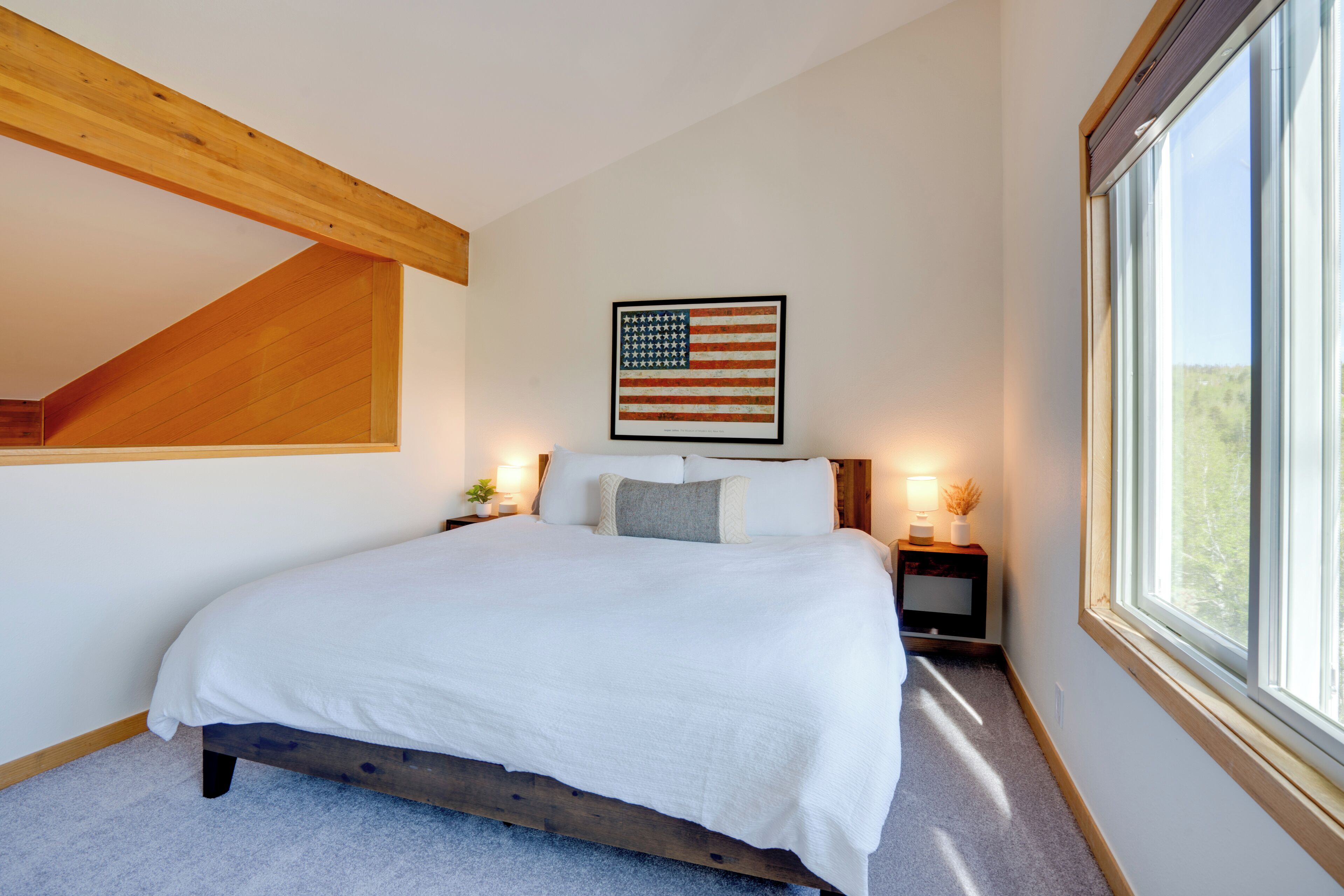 Una camera da letto con un letto, una bandiera americana incorniciata, un comodino con una lampada e una finestra.