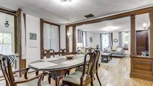 Uma área de refeições com uma mesa redonda, cadeiras de madeira e um sofá ao fundo.