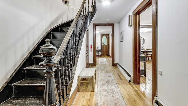 Uma escadaria com corrimão, um banco de madeira e um tapete que levam a um quarto com uma mesa de jantar e cadeiras.
