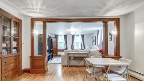 Um quarto amplo com piso de madeira, uma mesa de jantar com cadeiras, um sofá e um armário de madeira com gavetas.
