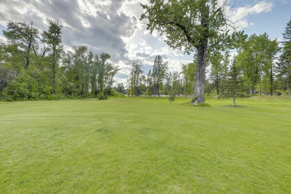 A grassy field with trees and a cloudy sky. - On the Flathead River! Rustic Saloon-Themed Cabin (Columbia Falls)