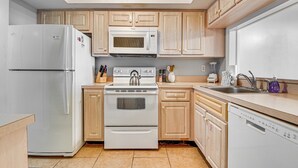 Eine Küche mit Holzausbau, einem weißen Kühlschrank, einer Mikrowelle, einem Backofen, einem Geschirrspüler und einem Waschbecken.