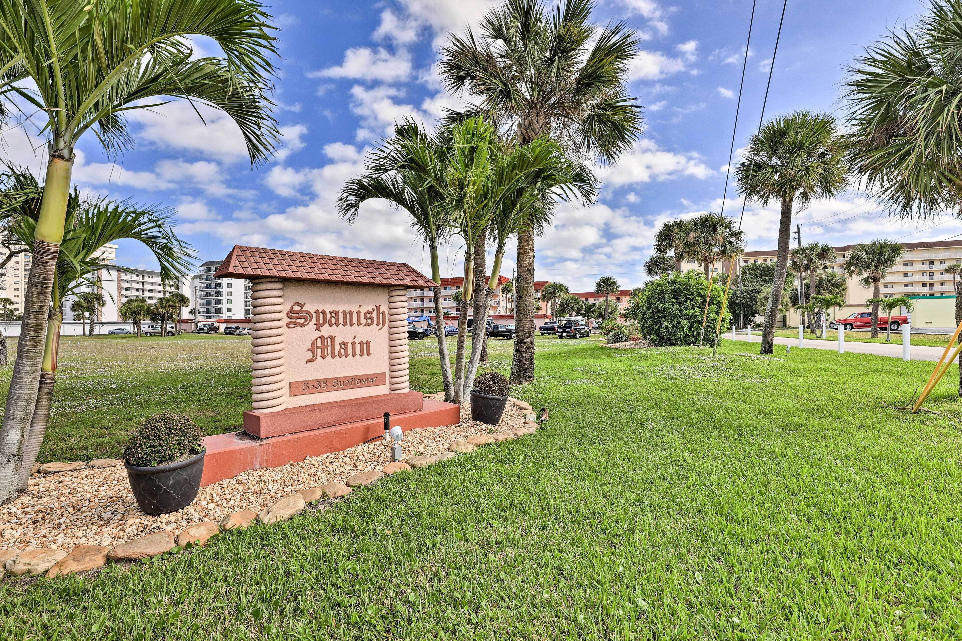 A sign with "Spanish Main" written on it, surrounded by palm trees and a grassy area.