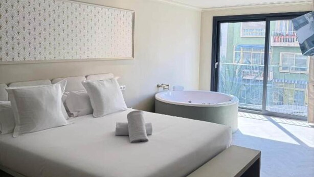 Ein Hotelzimmer mit einem großen Bett, einer runden Badewanne, einem Balkon mit Blick und einer Wand mit Muster.