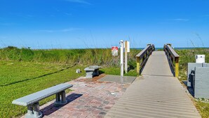 Una pasarela de madera que conduce al acceso a la playa, con un banco y un cartel.