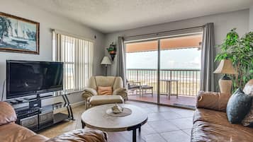 A living room with a TV, leather sofa, a round coffee table, a chair, and a balcony with a view.