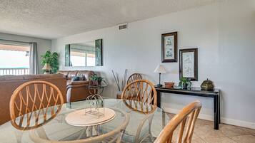 A dining area with a glass table, wicker chairs, a leather sofa, and a console table with decorative items.