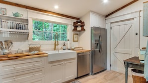 A kitchen with white cabinetry, a stainless steel refrigerator, a wooden countertop, and a window with a view of greenery.