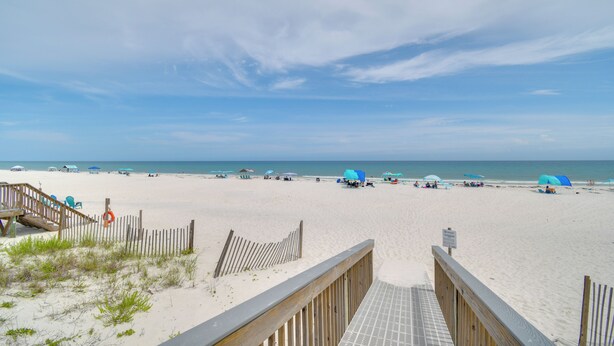 Une plage avec une promenade en bois menant à l’eau, des parasols et des chaises de plage.