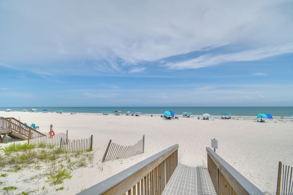 Ein Strand mit einer Holzpromenade, die zum Wasser führt, Sonnenschirmen und Liegestühlen.