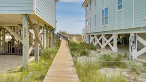 Une promenade en bois mène à des maisons de plage, avec une plage de sable et des dunes en arrière-plan.