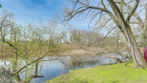 Una escena tranquil·la al costat d'un llac, amb arbres, una zona verda i un cel serè.