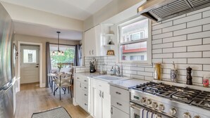 A modern kitchen with white cabinetry, a gas stove, a sink, and a window with a view of a building outside. - Premium Modern Midtown Favorite: Walk to it All! (Reno)