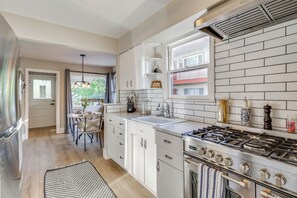 Een moderne keuken met witte kastjes, een gasfornuis en een raam met uitzicht op een balkon.