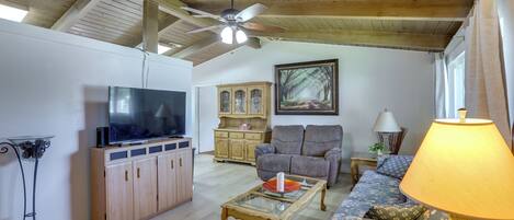 A living room with a television, wooden cabinets, a sofa, a coffee table, and a ceiling fan.