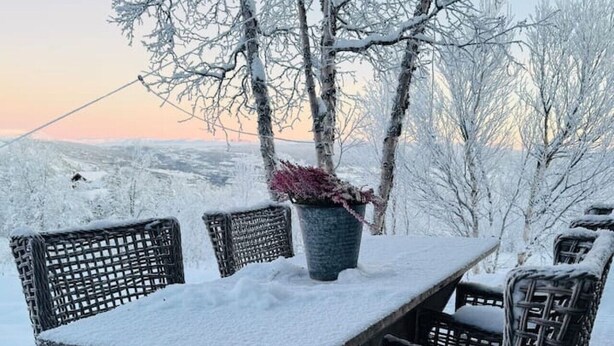 Ein mit Schnee bedeckter Essbereich im Freien mit Korbstühlen und einem Tisch, umgeben von Bäumen.