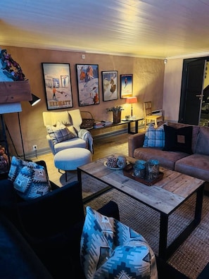 Ein gemütliches Wohnzimmer mit Sofa, Sesseln, Couchtisch und einem an der Wand befestigten Fernseher.