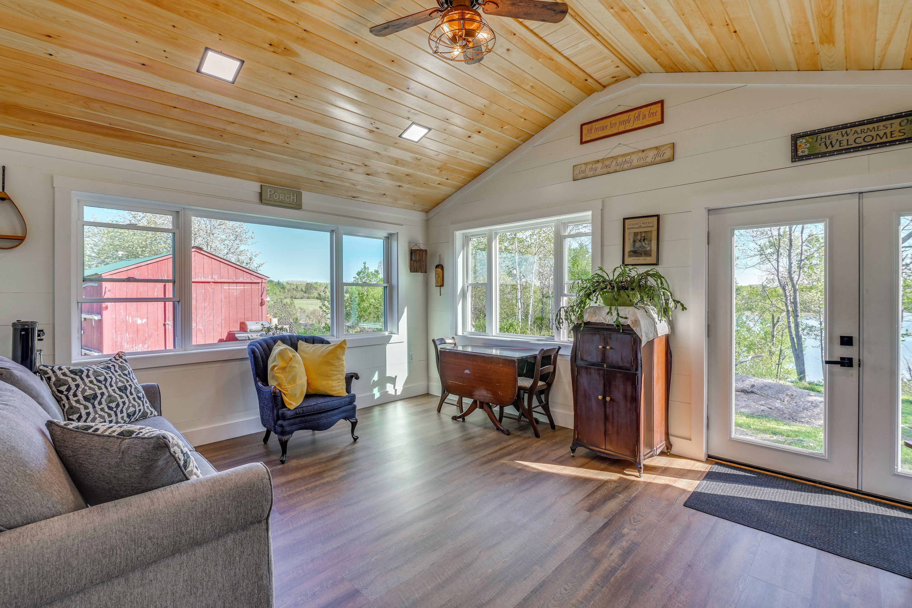 A spacious room with wooden floors, a dining table, a blue chair, a sofa, and a ceiling fan.