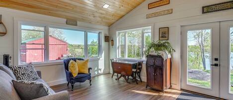 A spacious room with wooden floors, a dining table, a blue chair, a sofa, and a ceiling fan.