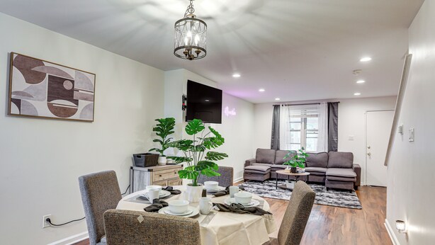 A dining area with a table set for four, surrounded by chairs, a chandelier, and a flat-screen TV mounted on the wall. - Groups & Pets Welcome! Spacious Philly Rowhouse (Philadelphia)