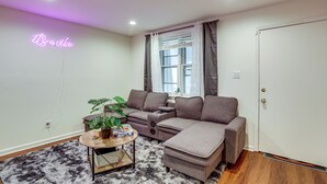 A living room with a sectional sofa, a coffee table with a plant, and a neon sign on the wall. - Groups & Pets Welcome! Spacious Philly Rowhouse (Philadelphia)