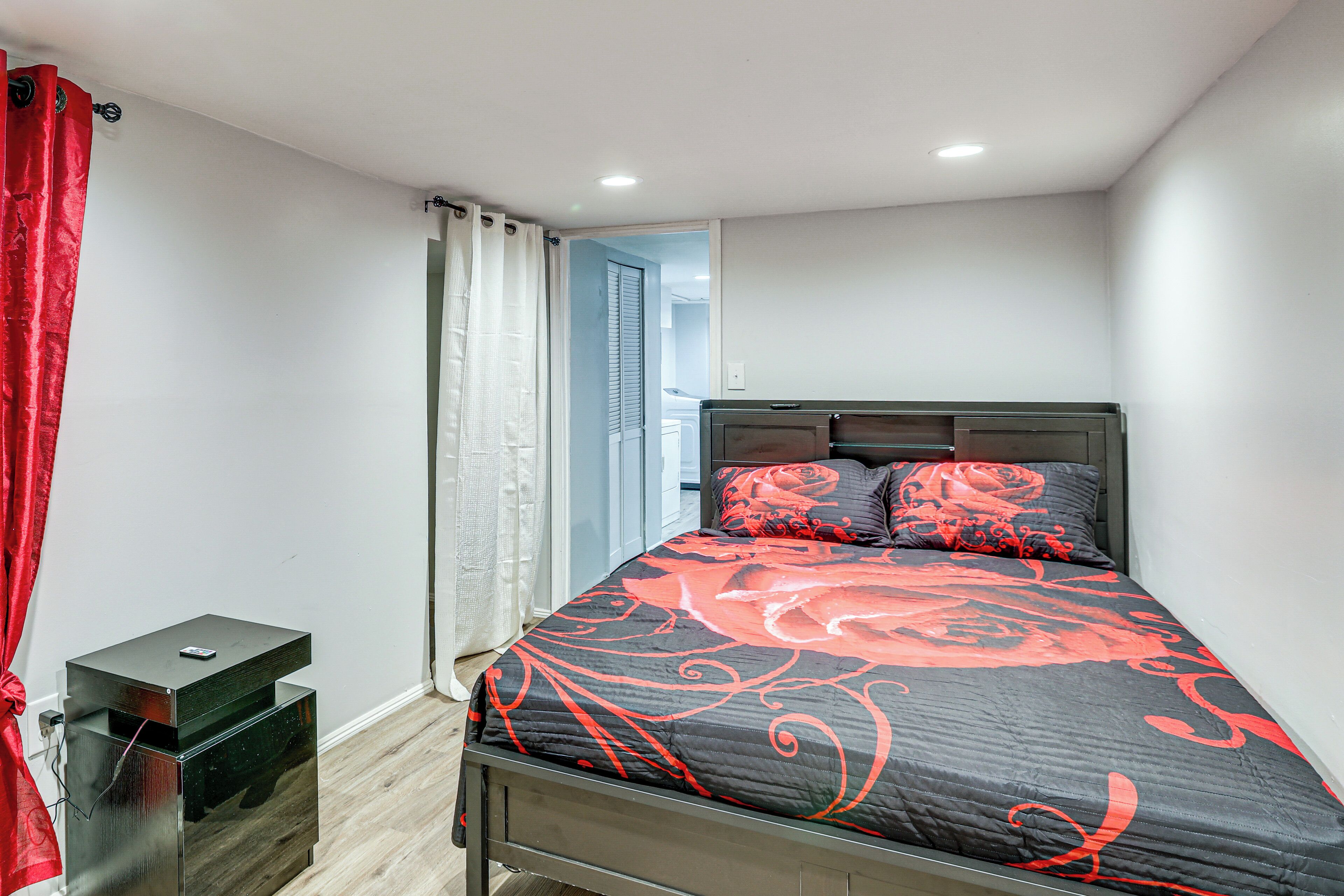 A bedroom with a bed, a nightstand, a red curtain, and a door leading to another room.