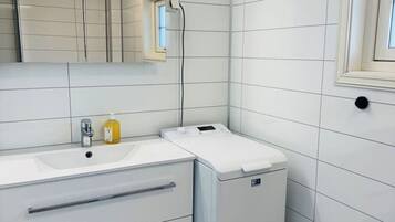 Een moderne badkamer met witte tegels, een wastafel, een spiegel, een verwarming en een prullenbak.