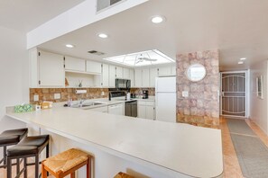 Eine moderne Küche mit weißen Schränken, einer großen Kochinsel mit Barhocker, einer Mikrowelle und einem Kühlschrank.