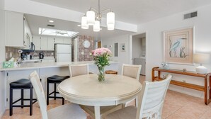 A modern kitchen with a dining area, a clock, and a vase with flowers. - Gulf-Front Gem w/ Pool Access on Fort Myers Beach! (Fort Myers Beach)