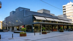 A modern building with a storefront, outdoor seating, and planters. - Deluxe Apartment with Balcony for 2 (Alicente)