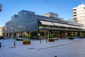 A modern building with a storefront, outdoor seating, and planters. - Deluxe Apartment with Balcony for 2 (Alicente)