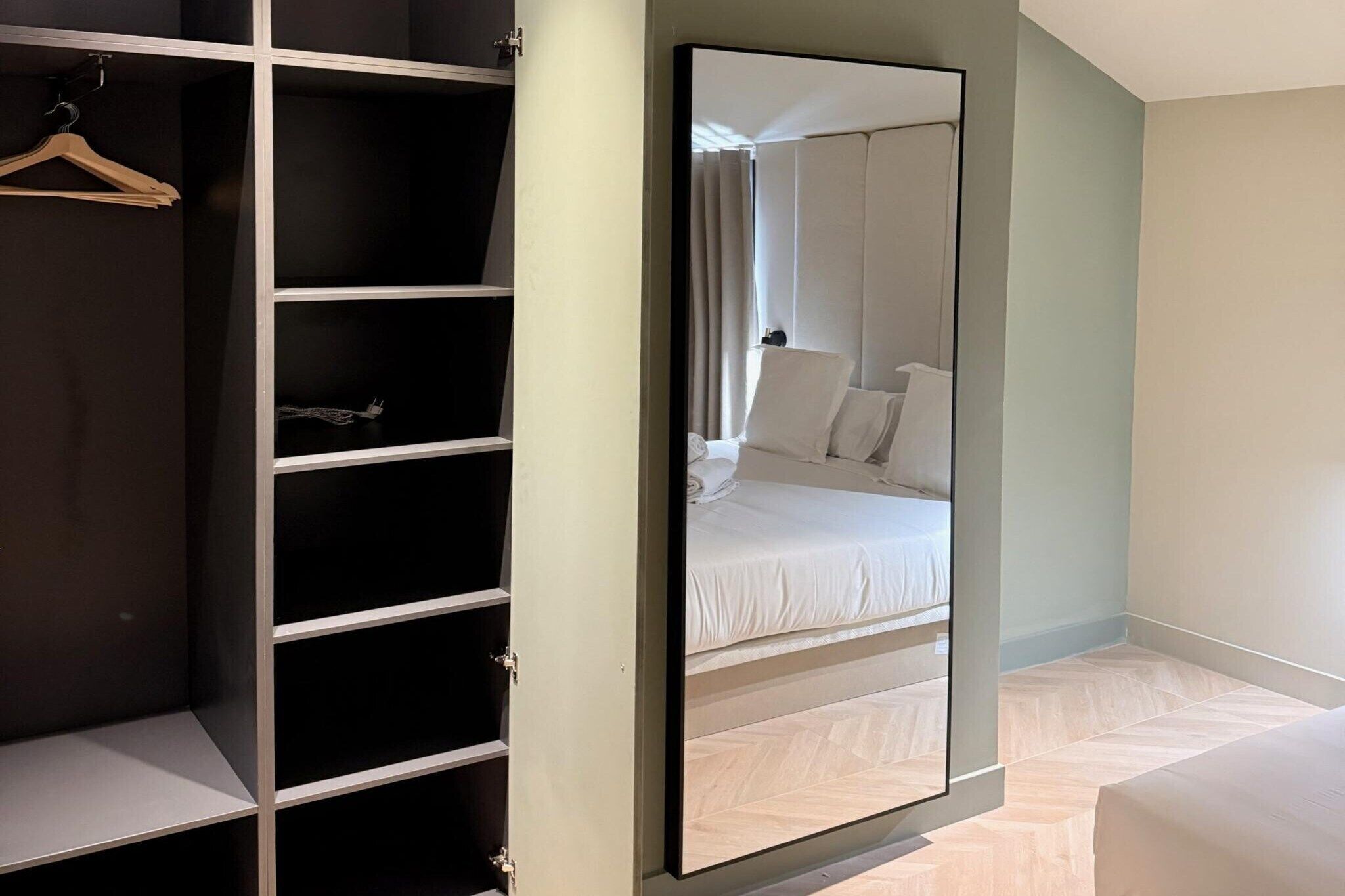 Ein Schlafzimmer mit einem großen Spiegel, einem Bett und einem Kleiderschrank mit vielen Regalen.