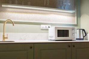 A kitchen with a gold faucet, a white microwave, and a coffee maker on the counter. - Deluxe Apartment with Balcony for 2 (Alicente)