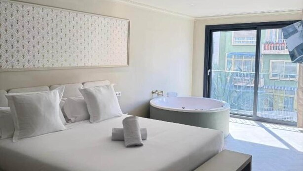 A hotel room with a bed, a bathtub, and a balcony with a view. - Deluxe Apartment with Balcony for 2 (Alicente)