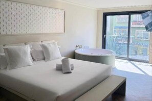 A hotel room with a bed, a bathtub, and a balcony with a view. - Deluxe Apartment with Balcony for 2 (Alicente)