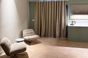 A room with a tufted armchair, a round table, a curtain, a sink, and a cabinet. - Deluxe Apartment with Balcony for 2 (Alicente)