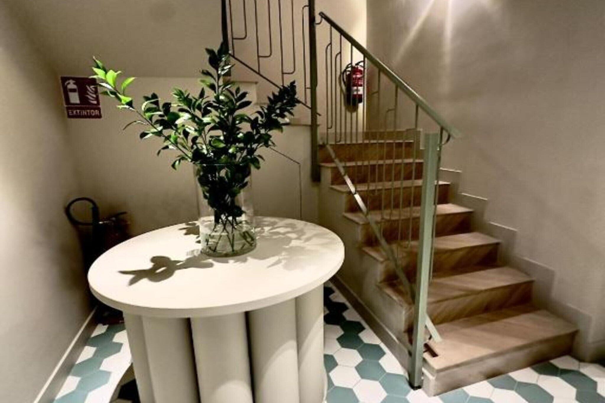 A staircase with a metal railing, a potted plant on a round table, and a fire extinguisher mounted on the wall.