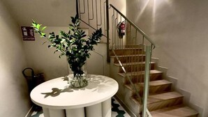 A staircase with a metal railing, a potted plant on a round table, and a fire extinguisher mounted on the wall. - Deluxe Apartment with Balcony for 2 (Alicente)