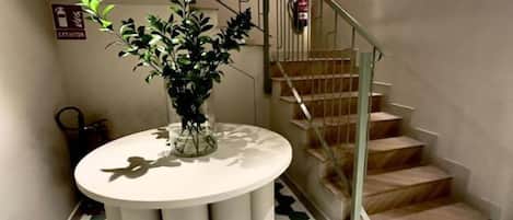 A staircase with a metal railing, a potted plant on a round table, and a fire extinguisher mounted on the wall.