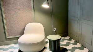 A room with a white chair, a floor lamp, a small stool, and a patterned floor. - Deluxe Apartment with Balcony for 2 (Alicente)