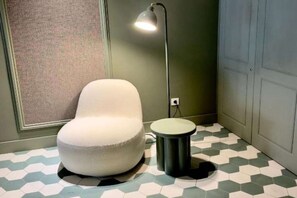 A room with a white chair, a floor lamp, a small stool, and a patterned floor. - Deluxe Apartment with Balcony for 2 (Alicente)