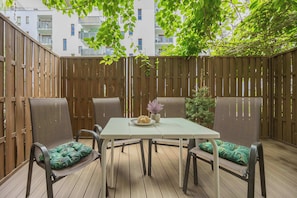 A patio with a table and chairs, surrounded by a wooden fence, with a view of buildings in the background. - Cosy Studio with Garden | Parking | Fan (Warszawa)